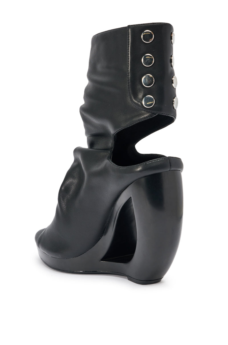 The AZALEA WANG CIRCOS BLACK WEDGE BOOTIE features a curved wedge heel, open back, slouchy ankle-high black upper, and five silver button-like studs along the side.