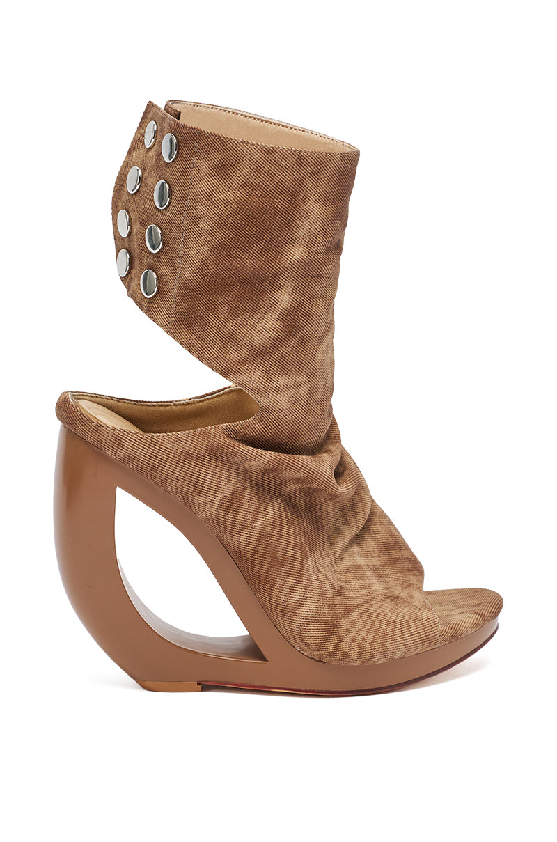 The AZALEA WANG CIRCOS BROWN WEDGE BOOTIE features a brown, open-toe ankle-high design, sculptural curved wedge heel, slouchy studded ankle cuff, and suede-like finish.