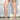 A person outdoors shows bare legs and feet in AZALEA WANG CLAREN BROWN MULTI WOODEN HEEL SANDALS, paired with a light ruffled skirt against a white wall and concrete ground.