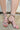 A person models the AZALEA WANG CLAREN BROWN MULTI WOODEN HEEL SANDAL, featuring strappy faux snakeskin and a square wooden block heel, standing on rough outdoor concrete with red-painted toenails for a chic look.