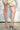 A person wearing a cream skirt and the AZALEA WANG CLAREN BROWN MULTI WOODEN HEEL SANDAL stands on a sunlit concrete surface in front of a white textured wall.