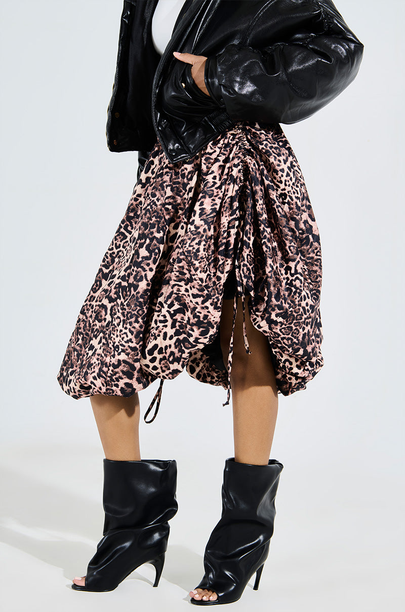 Dressed in a black faux leather jacket and a voluminous leopard print skirt, a person completes the stylish and edgy look with AZALEA WANG CLASSIE BLACK OPEN TOE BANANA HEEL BOOTIES. The ensemble is daring, combining bold prints with rich textures.