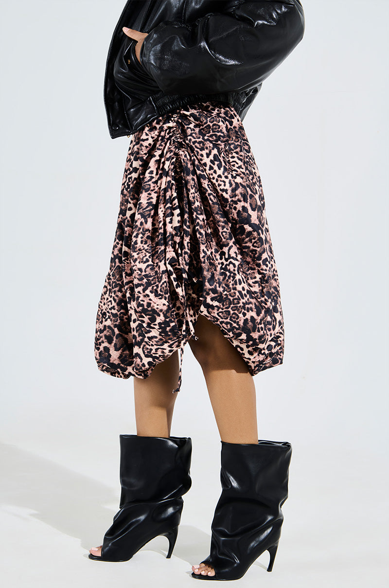 A person in a black faux leather jacket and pink leopard-print skirt stands with hands in pockets, sporting the AZALEA WANG CLASSIE BLACK OPEN TOE BANANA HEEL BOOTIE against a plain white background.