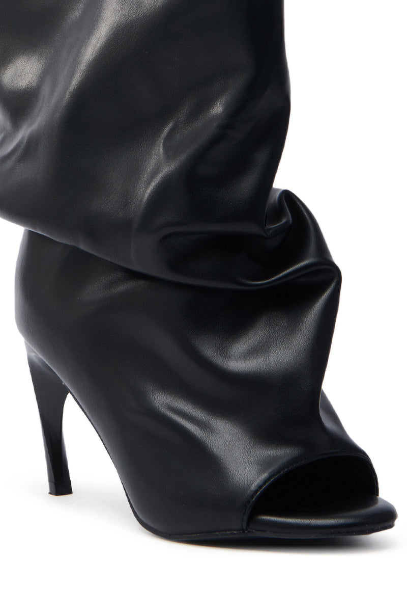 Close-up of the AZALEA WANG CLASSIE BLACK OPEN TOE BANANA HEEL BOOTIE, a black faux leather high-heeled boot featuring a slouchy and open-toe design with soft, shiny material elegantly draping above the ankle and a slender, slightly tapered banana heel.
