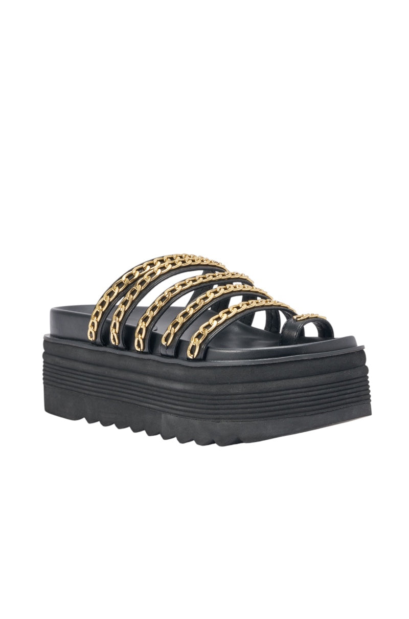 The AKIRA CLEMENTE GOLD CHAIN DETAIL FLATFORM SANDAL is a black faux leather sandal with four thick straps featuring gold chain accents and a chunky ridged sole. 4