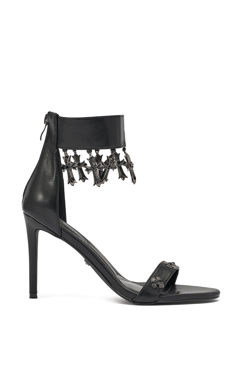 The AKIRA GOLD CLERGY BLACK EMBELLISHED SEXY STRAP STILETTO HEEL features a black cross ankle strap, metallic charms, and a thin toe strap—shown in side profile on a white background for a bold, gothic-inspired statement. 2