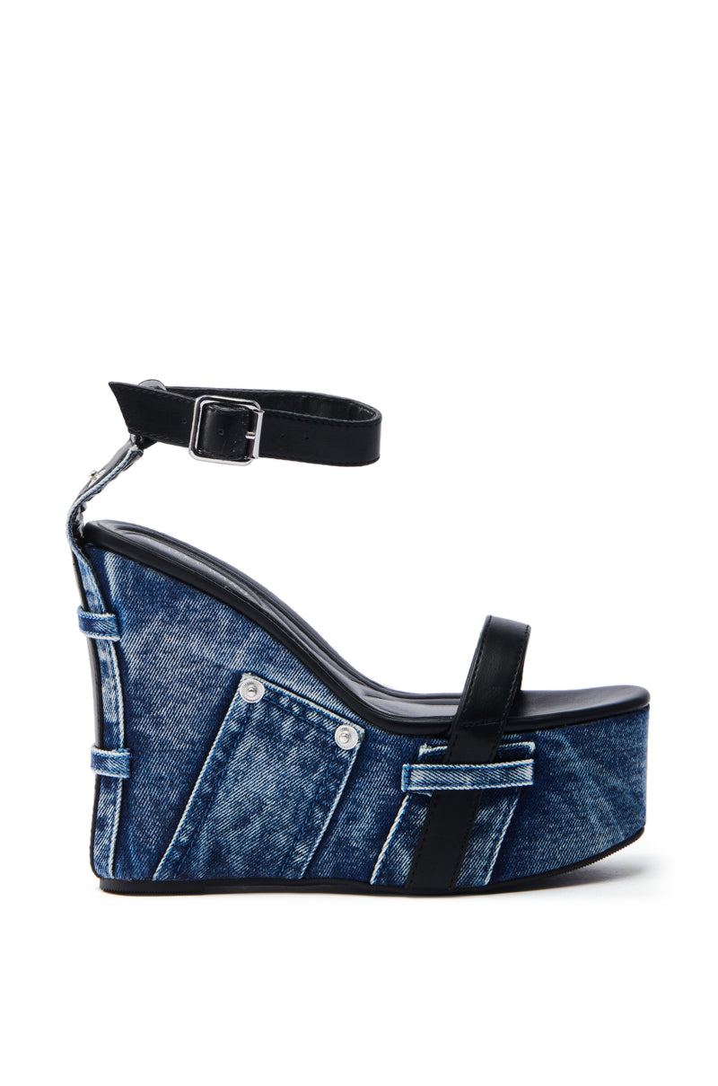 The AZALEA WANG CLIO DENIM SANDAL is a high wedge heel sandal with jean-inspired design, featuring visible seams and button details. It has black leather straps, an ankle strap with a silver buckle, and a sturdy platform sole.