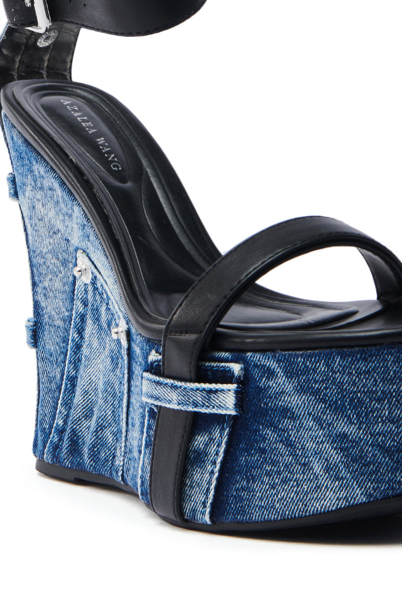 A close-up of AZALEA WANG CLIO DENIM SANDAL features chic blue denim fabric on the platform sole and wedge heel, with elegant black leather straps crossing over the foot and a visible logo on the insole.
