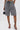 A person wears SHAGGY BERMUDA SHORTS in a two-tone design, black ankle-strap high heels, and holds a small black handbag against a plain white background.