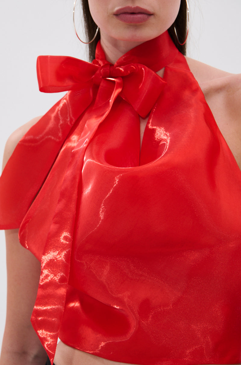 A woman wears large hoop earrings and the SUNSHINE COWL NECK SATIN BLOUSE IN ORANGE, featuring a shiny finish and a decorative bow at the neck. Her face is partially visible.