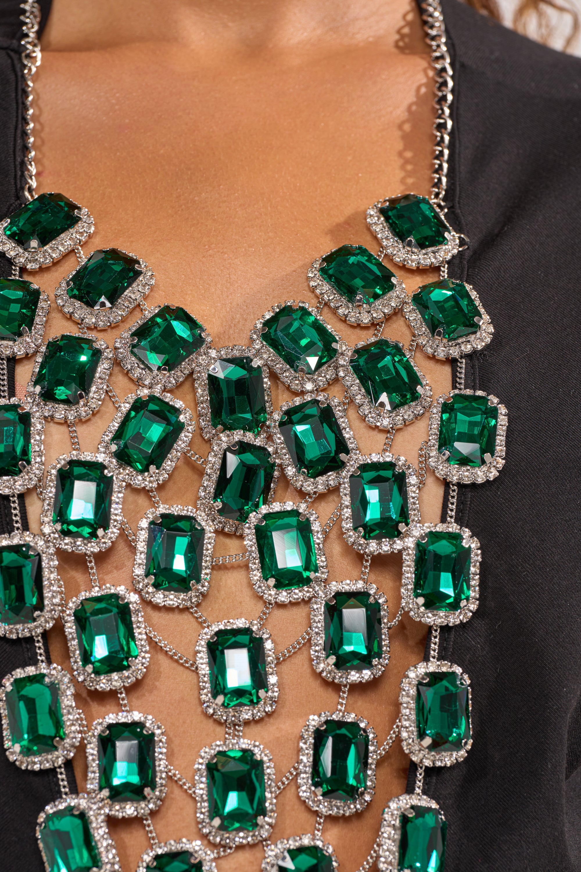A close-up of a person wearing the EMERALD BABY RHINESTONE TEE, featuring sparkling rectangular green rhinestones set in silver, forming a bold necklace design that covers the chest for standout streetwear. 6