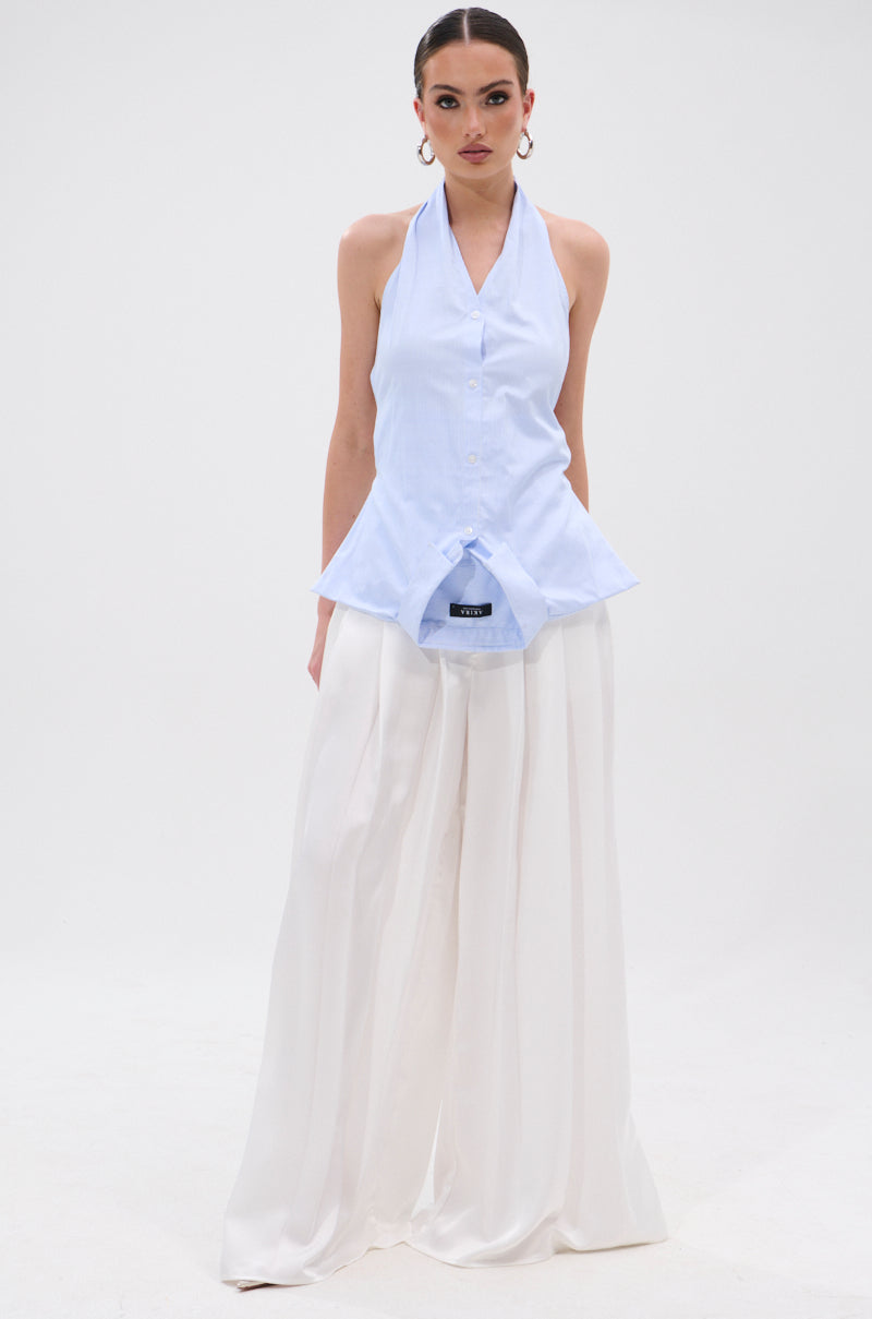 A woman wears the TINA STRIPE POPLIN BLOUSE—a sleeveless, light blue pinstriped halter top with front buttons—paired with high-waisted, wide-leg white pants. She stands against a plain white background. 5