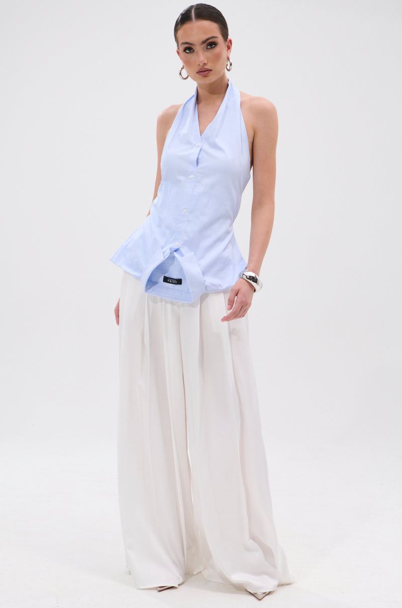 A woman poses against a white background wearing the TINA STRIPE POPLIN BLOUSE, styled with wide-legged white pants, hoop earrings, a watch, and slicked-back hair. 6