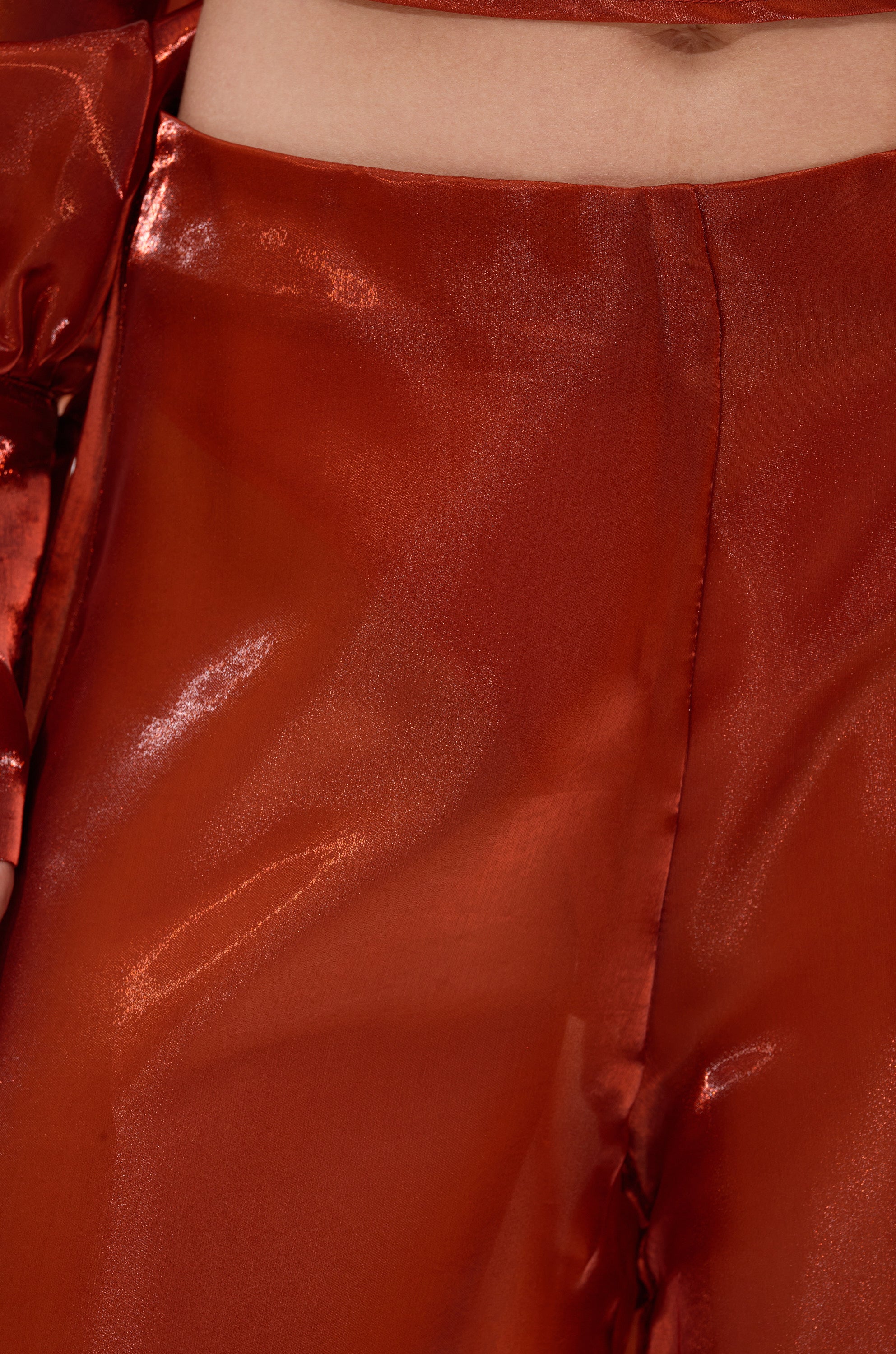 Close-up of a person wearing FEELING FREE CHIFFON PALAZZO PANT in shiny, metallic red with a high waist and visible center seam. The light-reflecting fabric gives glossy highlights and a smooth finish. 4