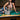 A woman in the SHAKE IT FOR ME BABY BEADED BLOUSE and ripped jeans sits on a pool table, with a silver jeweled handbag nearby against an exposed brick wall.