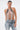 A woman with dark hair in a sleek bun poses against a plain white background wearing the SHAKE IT FOR ME BABY BEADED BLOUSE, an open-back top with cascading beads, paired with distressed blue lace-up jeans.