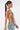 A woman with long, straight dark hair in a ponytail models the SHAKE IT FOR ME BABY BEADED BLOUSE—a silver glass beaded halter top—with light blue lace-up jeans, posing in profile against a plain white background.