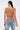 A woman with long dark hair in a ponytail is shown from the back, wearing the SHAKE IT FOR ME BABY BEADED BLOUSE with thin straps and light blue jeans featuring white lace-up details on one pocket.
