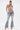 A woman poses in the SHAKE IT FOR ME BABY BEADED BLOUSE with cascading glass strands, paired with light-wash flared jeans featuring crisscross lace-up details, silver high-heeled sandals, and slicked-back hair.
