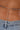 Close-up of a person’s lower back wearing the SHAKE IT FOR ME BABY BEADED BLOUSE, styled with light blue denim jeans. The blouse's gunmetal seed bead details rest above the jeans against tan skin.
