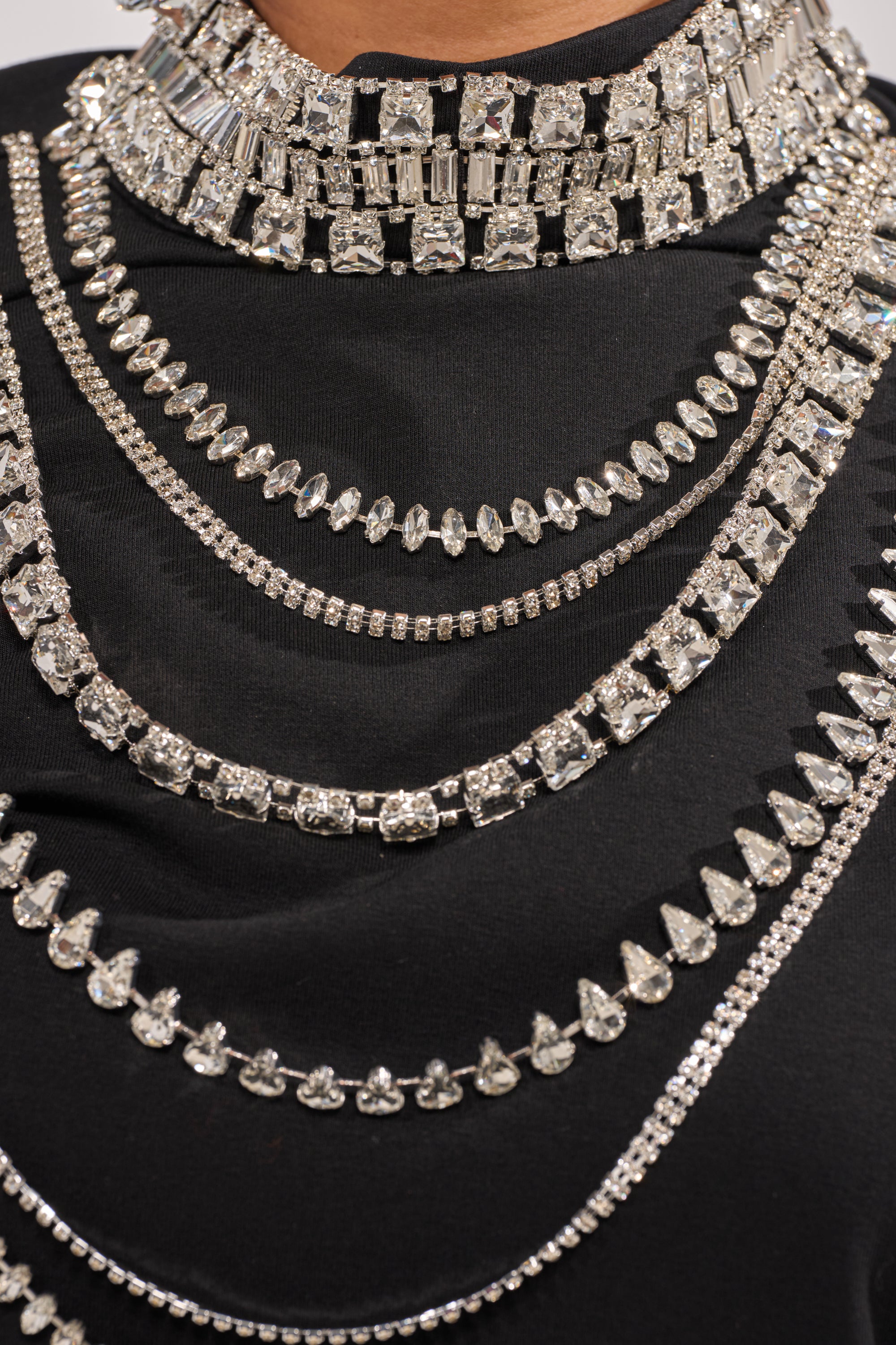 A close-up of a person wearing the ROYALTY RHINESTONE TEE, styled with layered sparkling silver rhinestone necklaces and a bold, ornate rhinestone choker. 6
