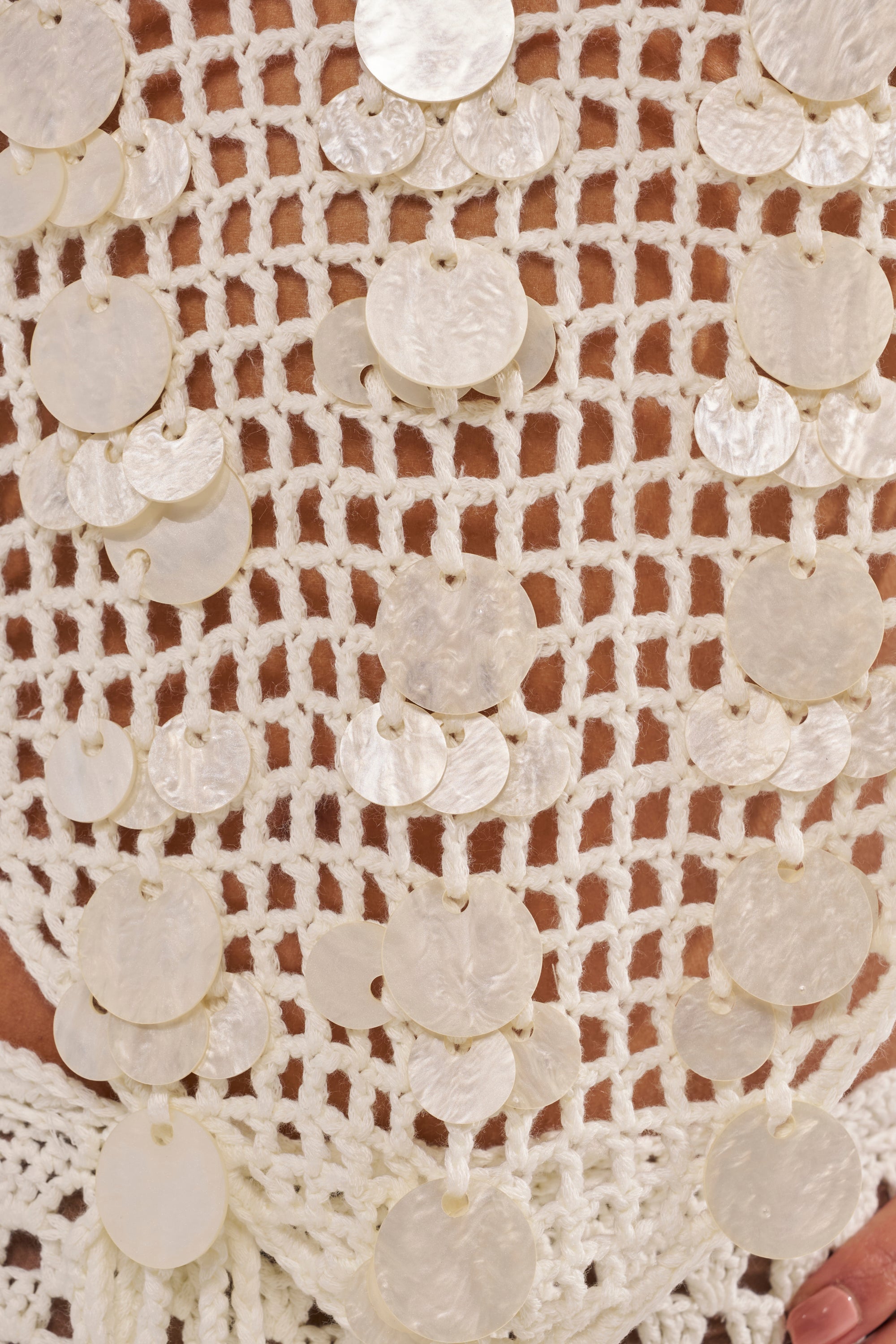 Close-up of the TAKE ME TO THE CLUB CROCHET TANK, a white crocheted halter top featuring hanging iridescent sequin discs for a textured, decorative look—perfect for chic beach club style. 8