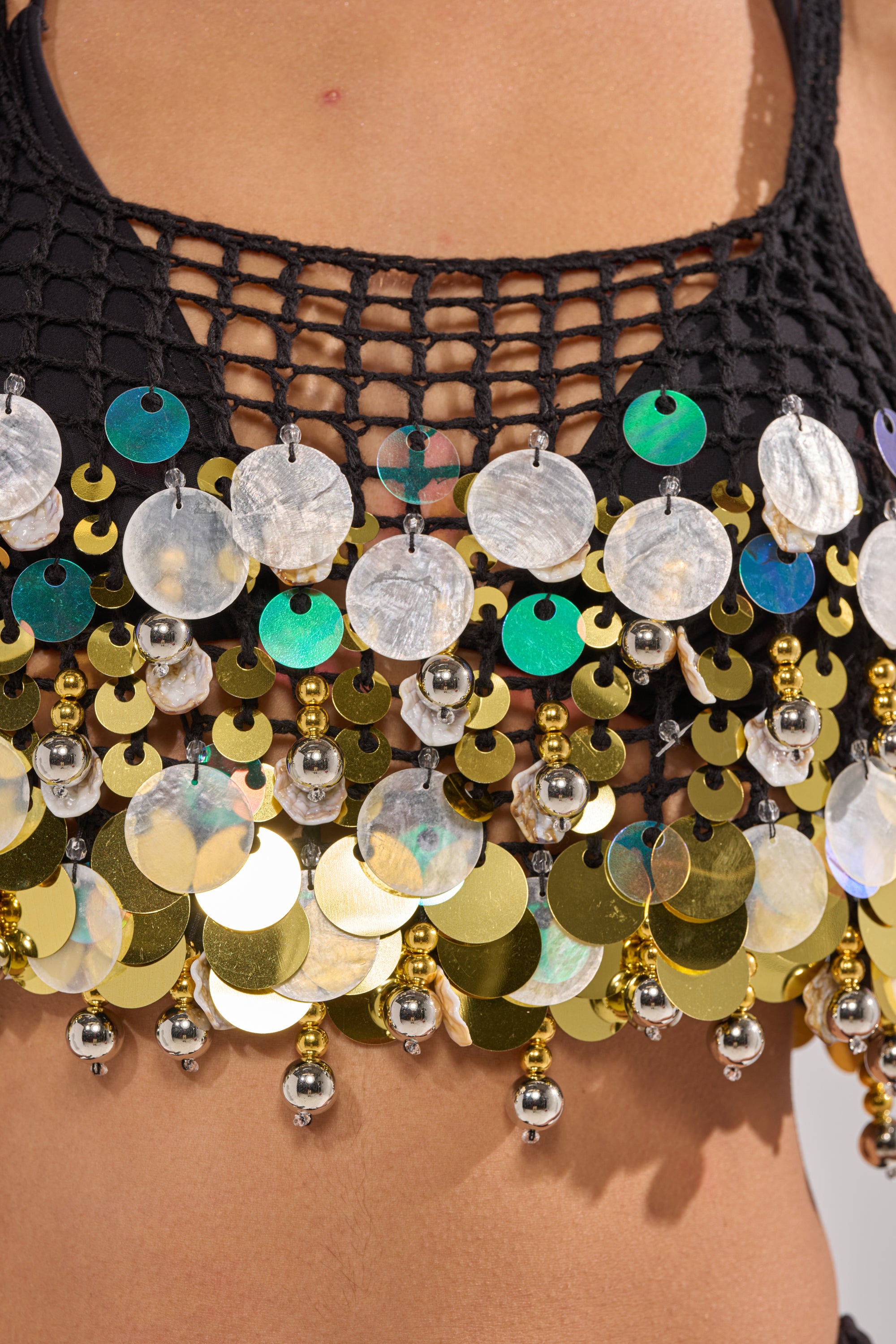 Close-up of the RESORT LIVING SEQUIN CROCHET TOP in black, featuring shiny gold, silver, and iridescent sequins with small metallic beads, worn on bare skin. 8