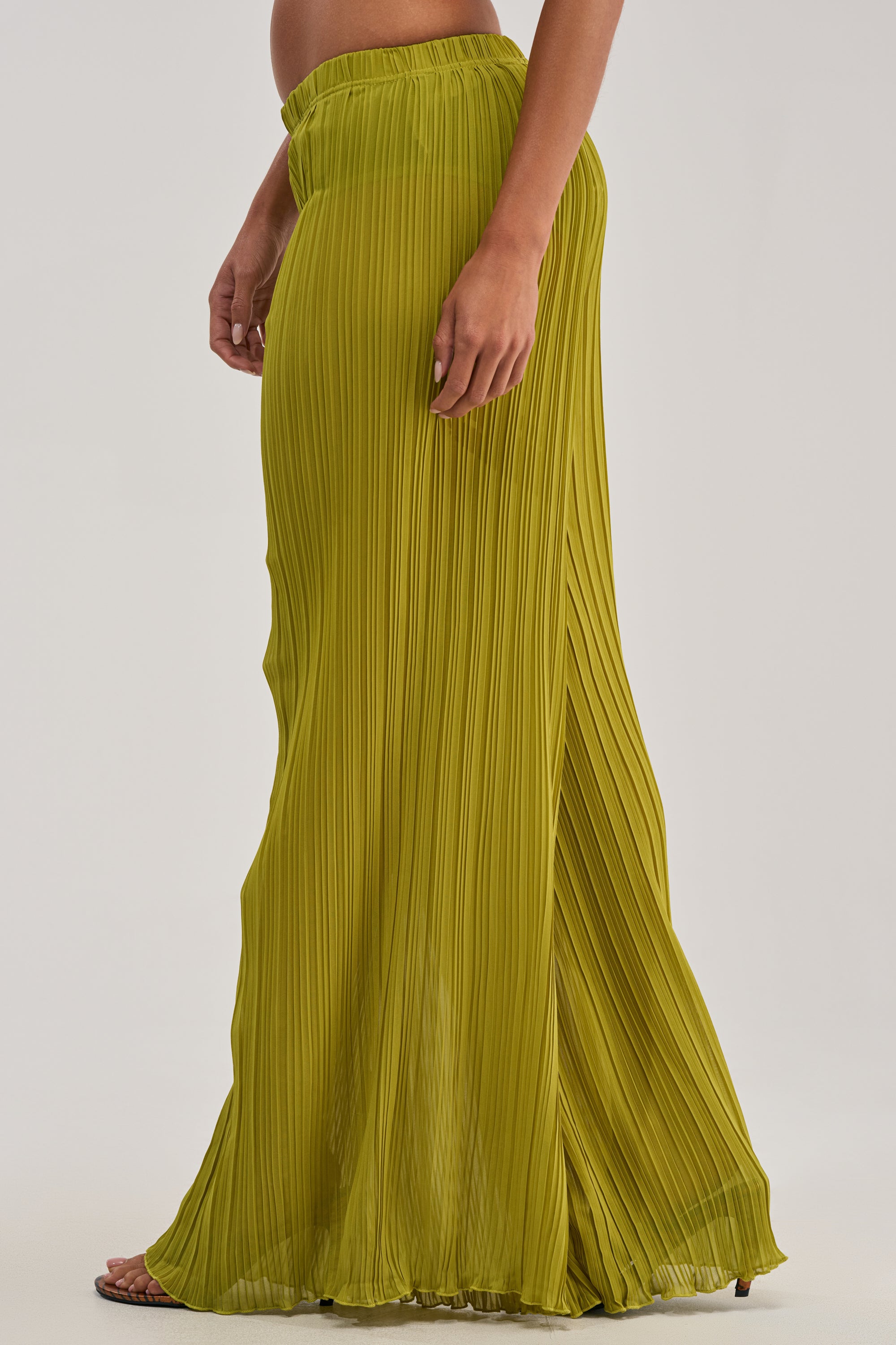 Barefoot on a plain background, the lower body is shown wearing CRUSHIN ON YOU PALAZZO PANT IN CHARTREUSE—pleated chiffon with an elastic waistband, showcasing a flowy, vibrant resort wear vibe.