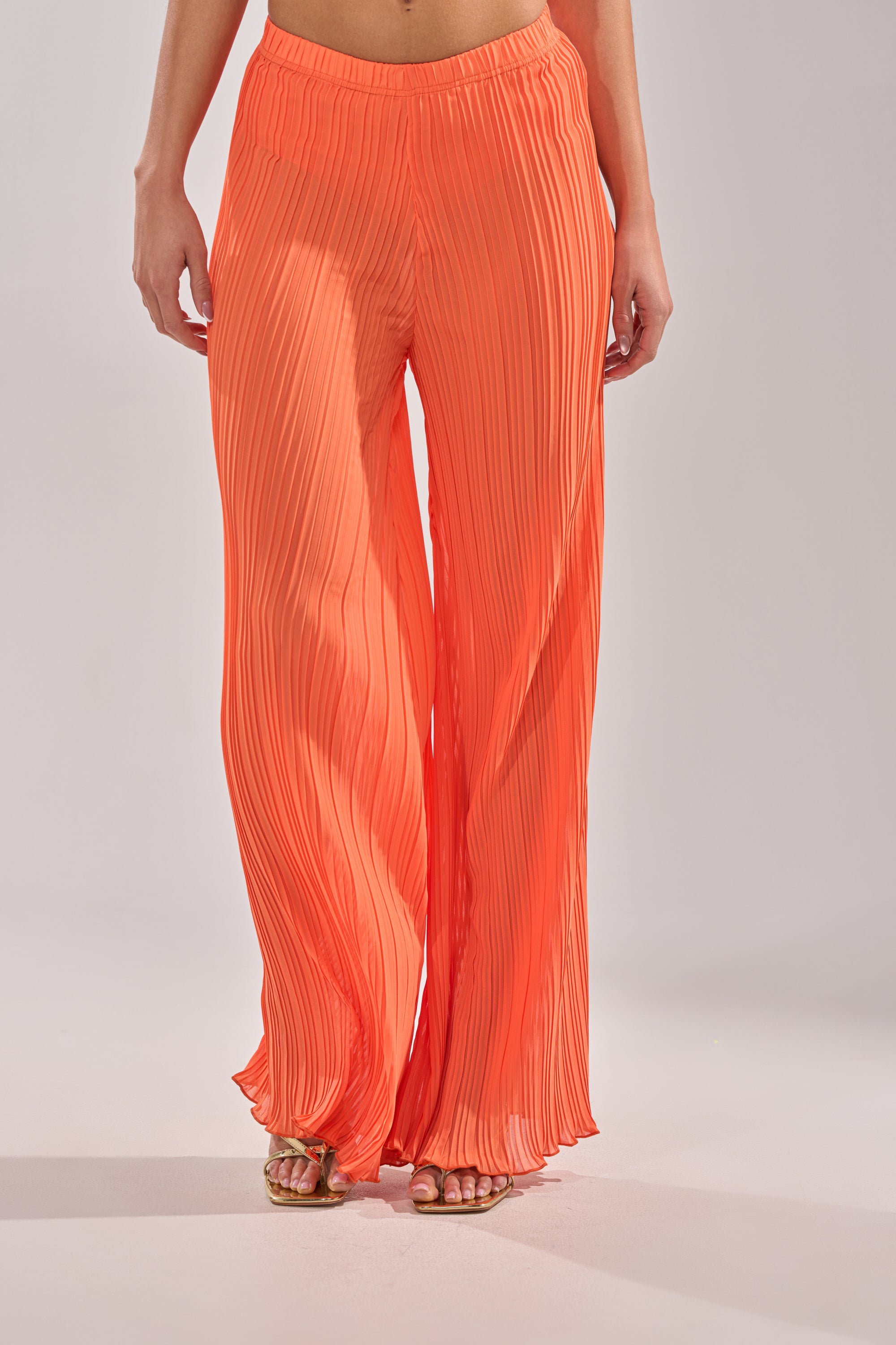 Wearing the CRUSHIN ON YOU PALAZZO PANT, wide-leg and high-waisted in bright orange, paired with open-toe sandals, this person stands against a plain light background. 2