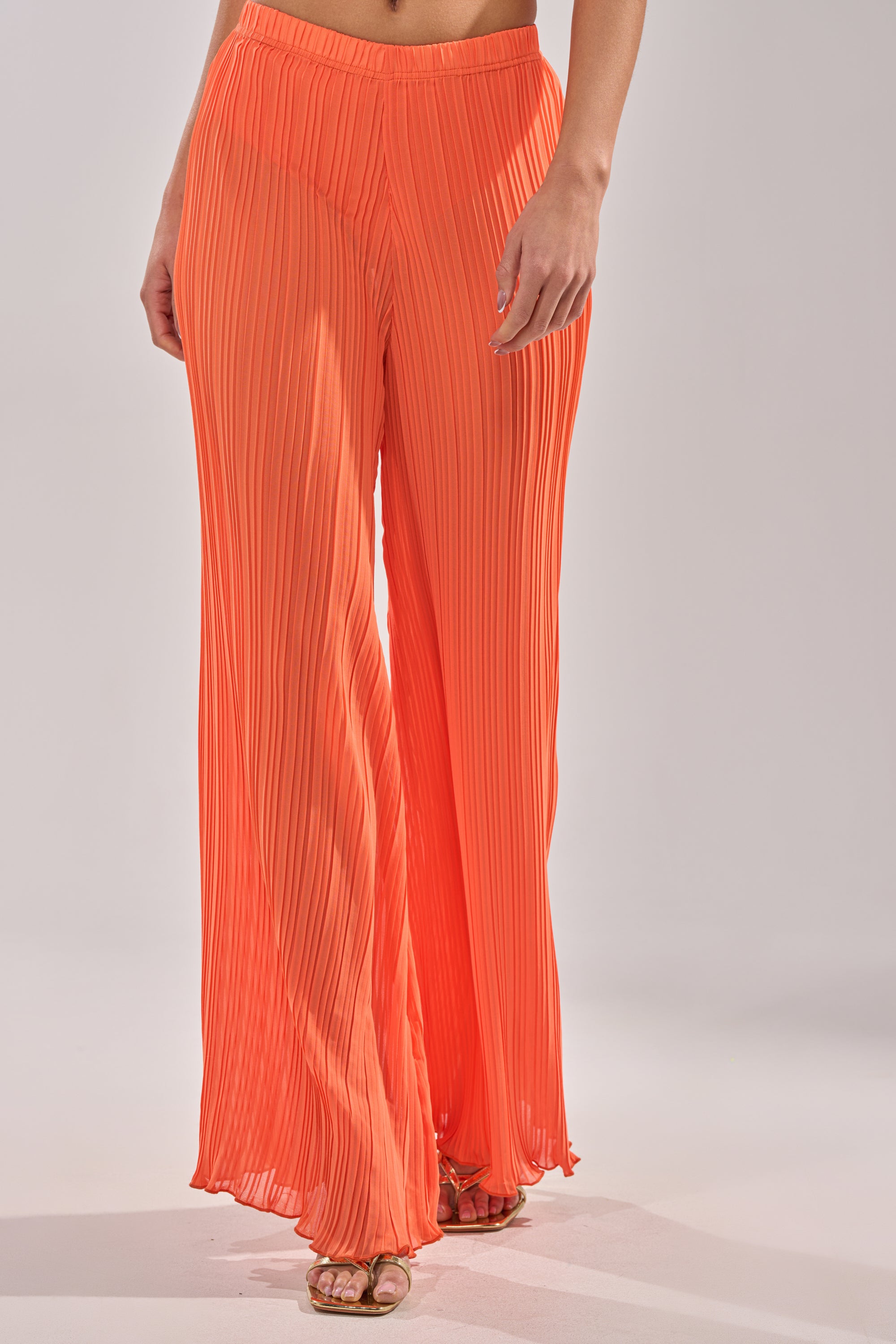 A person is seen from torso to legs wearing the CRUSHIN ON YOU PALAZZO PANT in orange—high-waisted, pleated, and flowy—making these wide-leg pants a vibrant, stylish addition to any vacation wardrobe. 3