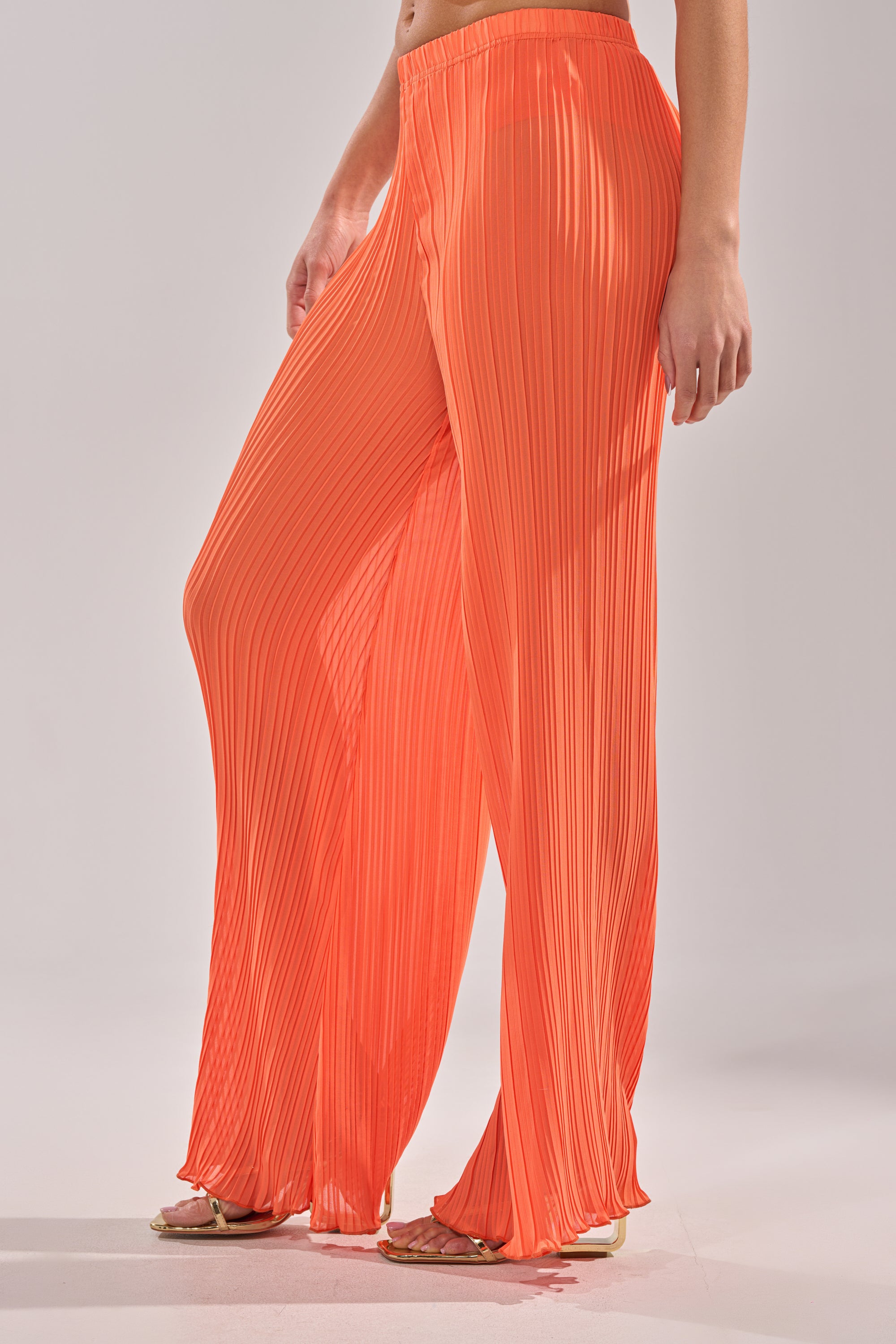 A person models the CRUSHIN ON YOU PALAZZO PANT—loose-fitting, high-waisted, and orange—paired with open-toe sandals against a plain light background, making it an ideal vacation wardrobe choice. 4