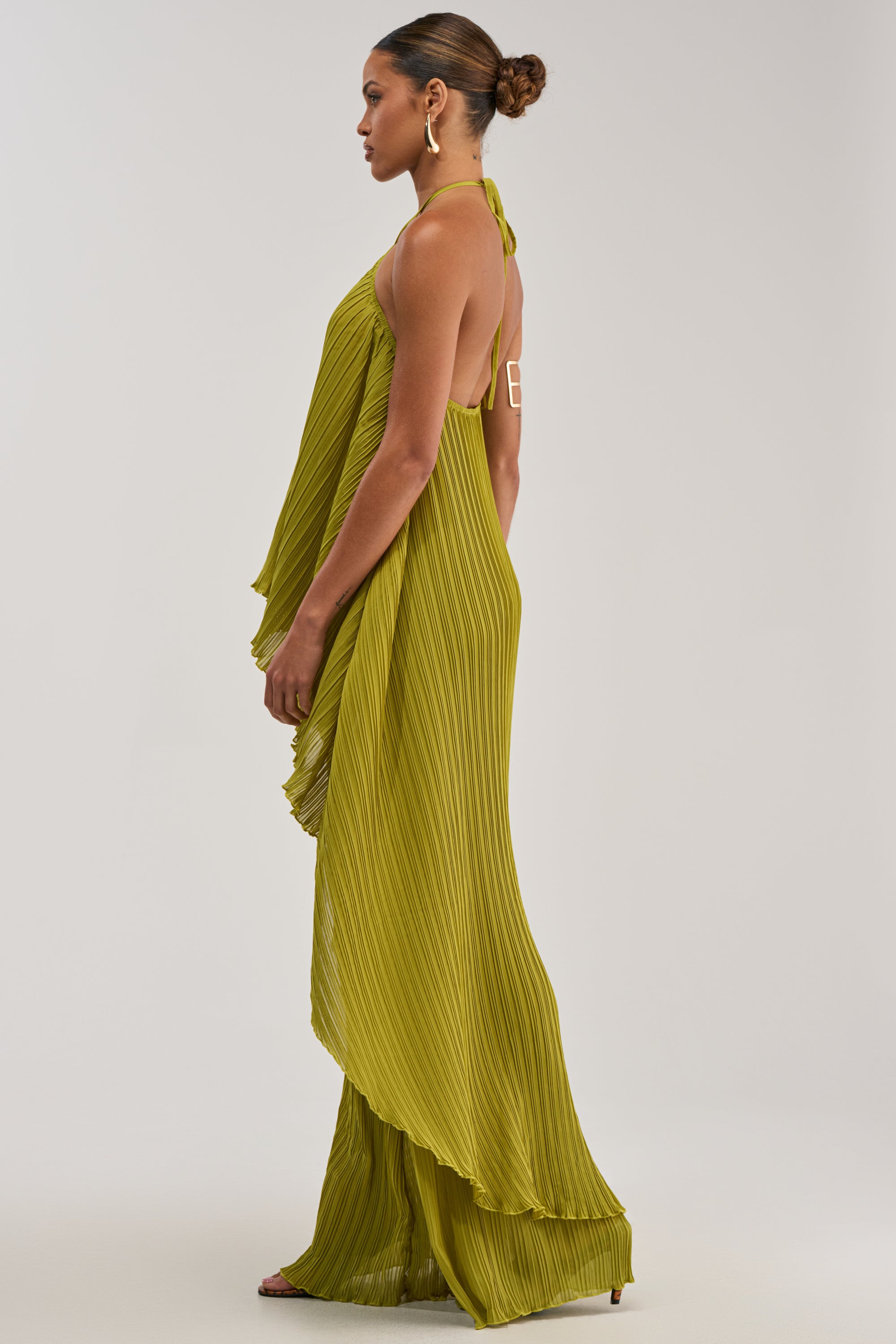 Woman in profile wears the CRUSHIN ON YOU BLOUSE IN CHARTREUSE with her hair in a neat bun, accessorized with large hoop earrings and strappy heels, set against a plain background.