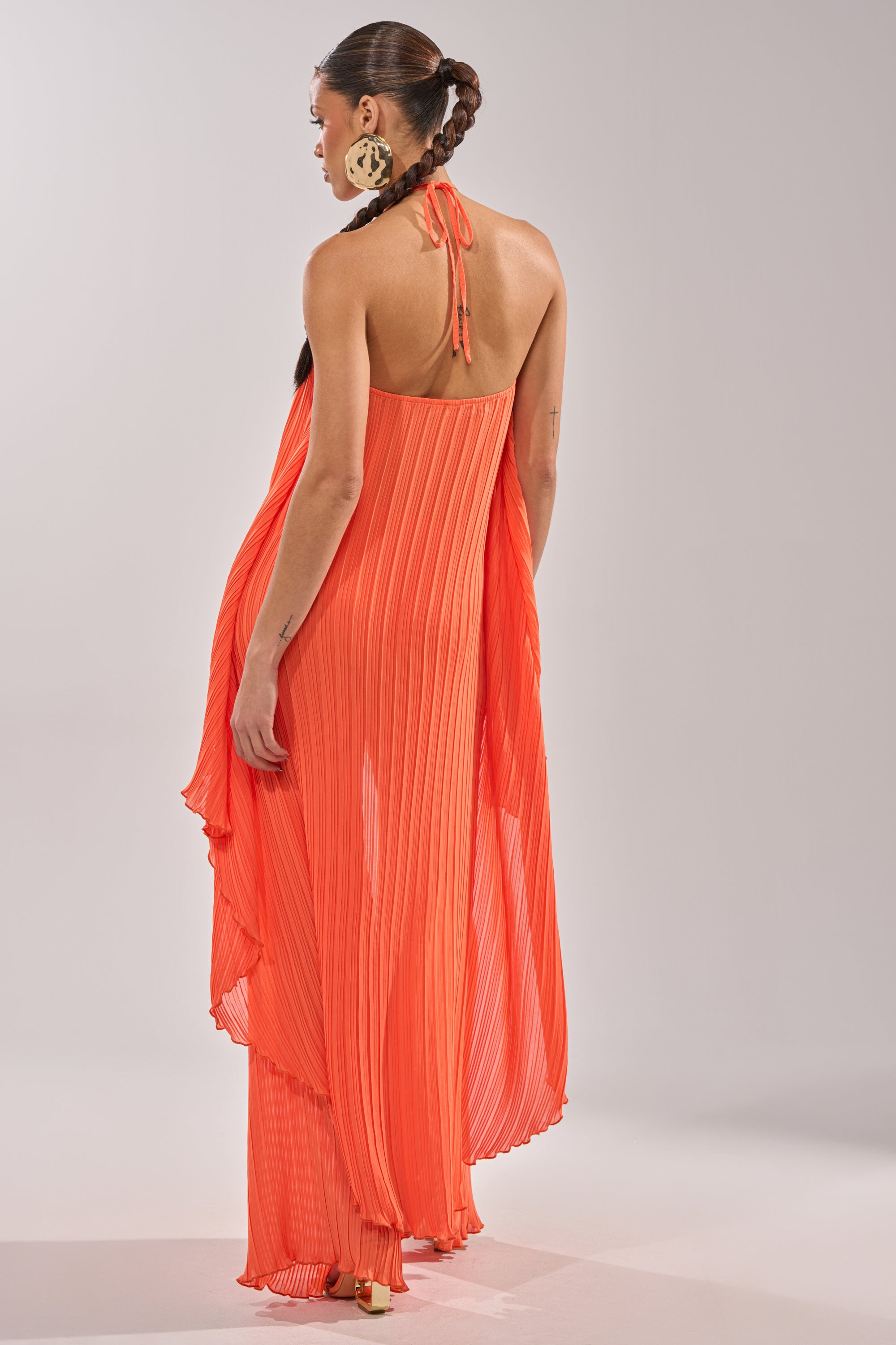 A woman with braided hair stands sideways against a plain gray background, wearing the bright orange CRUSHIN ON YOU BLOUSE and matching wide-leg pants, paired with large, round earrings. 10