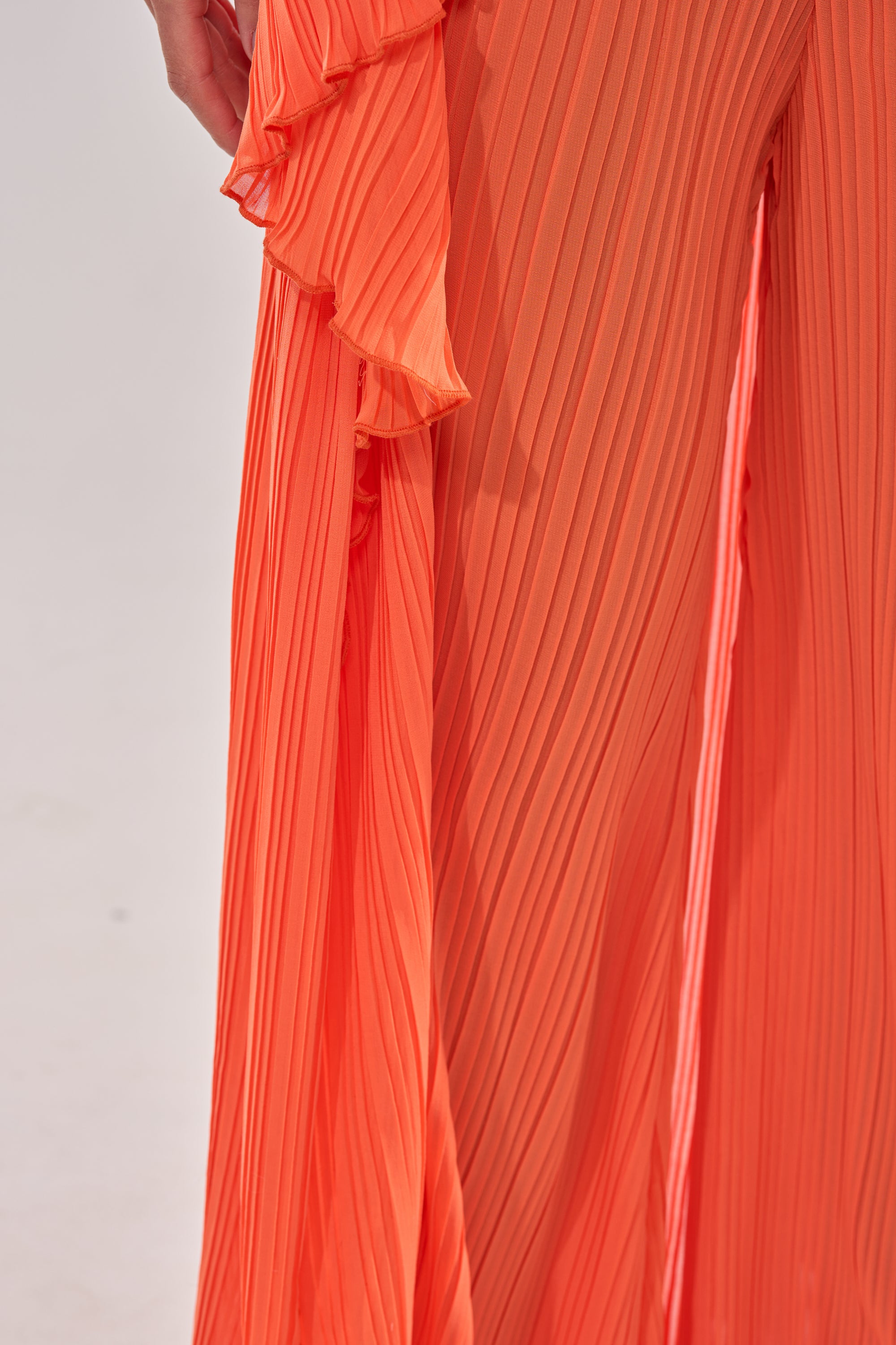 Close-up of a person wearing bright orange, pleated, flowy pants with ruffle detail and vertical ribbed texture, perfectly paired with the CRUSHIN ON YOU BLOUSE. The background is plain and light-colored. 12