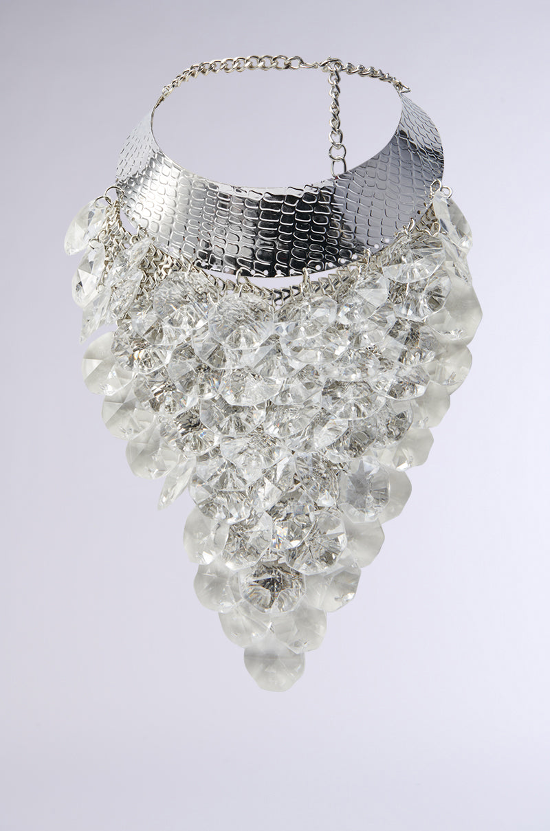 The PARTY STARTER LUXE NECKLACE features a wide silver textured collar with cascading triangle-shaped clear gems on short chains—an eye-catching statement piece. 0