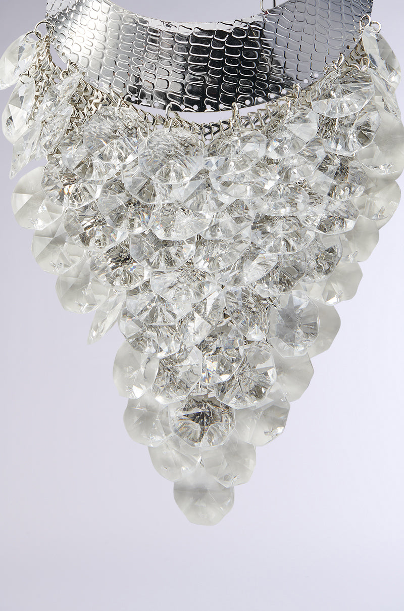 A close-up of the PARTY STARTER LUXE NECKLACE showcases its shiny silver mesh and dangling crystal-clear gems in a triangular, chandelier-inspired design. 2