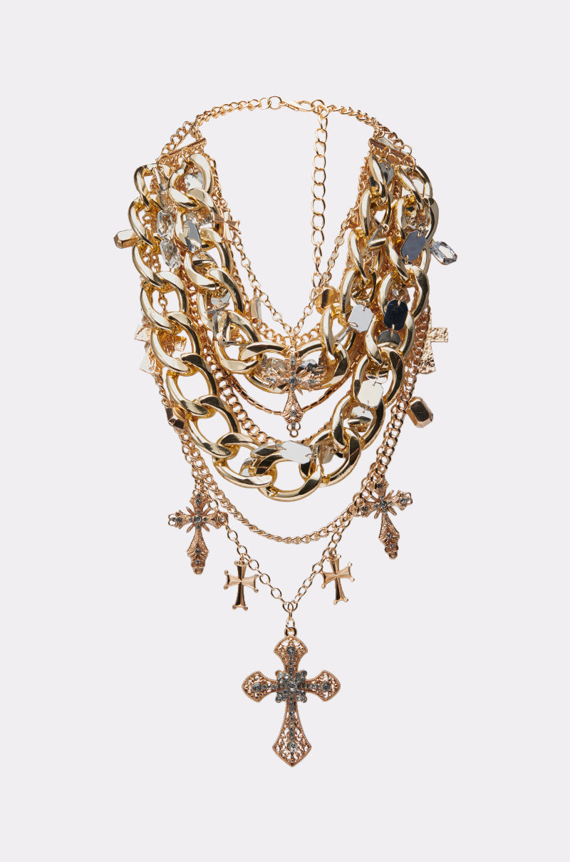 The CROSS ME NECKLACE IN GOLD features gold-tone layers, sparkling rhinestone accents, and multiple dangling cross pendants for a bold statement look.