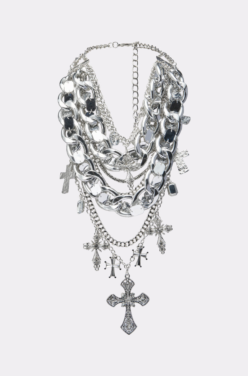 The CROSS ME METAL NECKLACE features layered chunky curb chains with multiple cross pendants, including rhinestone-encrusted designs of various sizes, displayed on a light gray background.