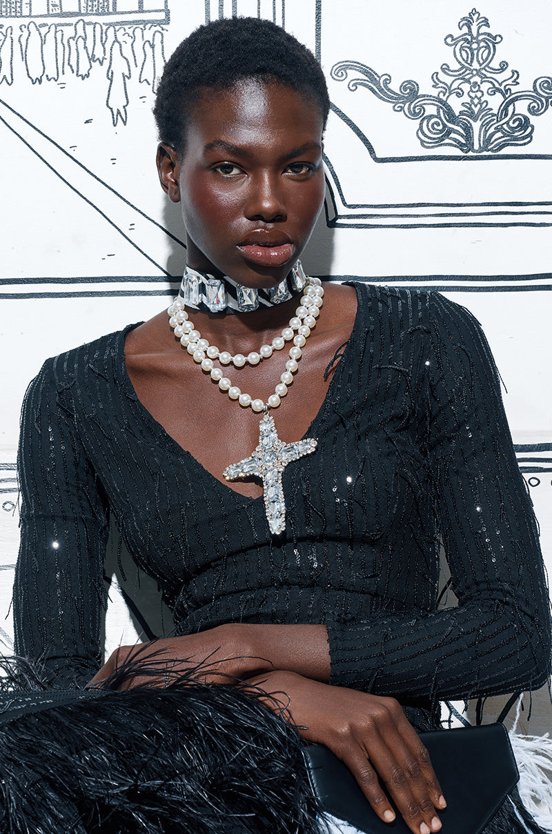 A person with short hair wears a black sequin dress and the WALK ON THE WILD SIDE STATEMENT NECKLACE, posing in front of an illustrated black-and-white background.