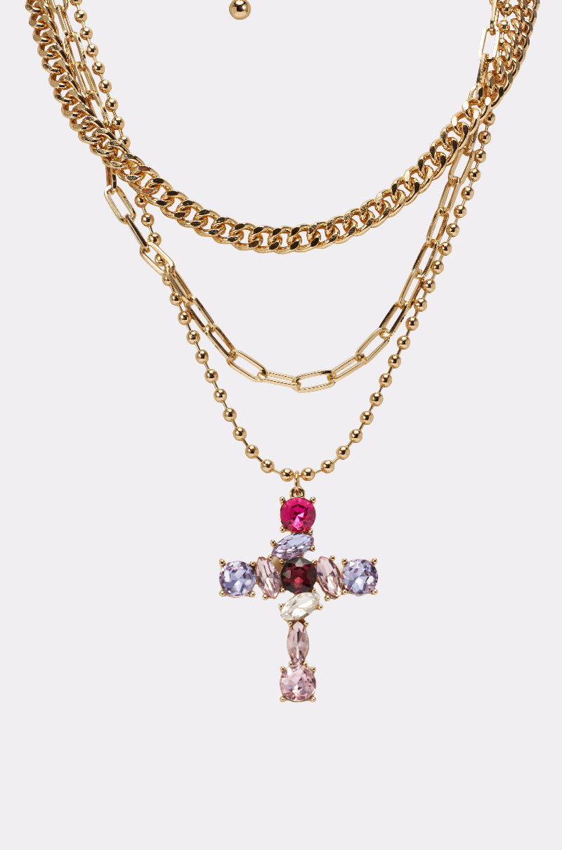 The JULIA NECKLACE is a gold layered chain necklace with a jeweled cross pendant adorned with pink, purple, and clear gemstones—an eye-catching statement piece that shines on any plain light background. 3