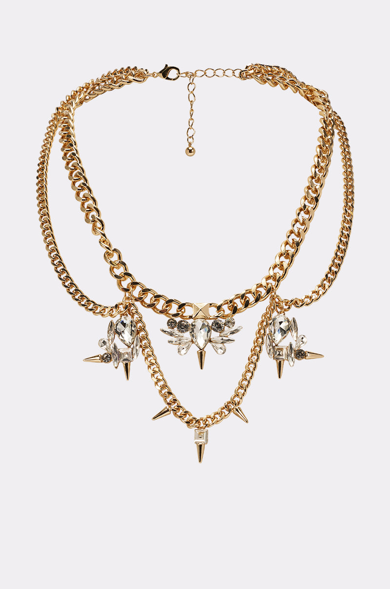The SPIKEY NECKLACE features layered gold chains with clear crystal flower accents and gold spike charms, shown on a plain white background—a stunning statement piece for any occasion. 0