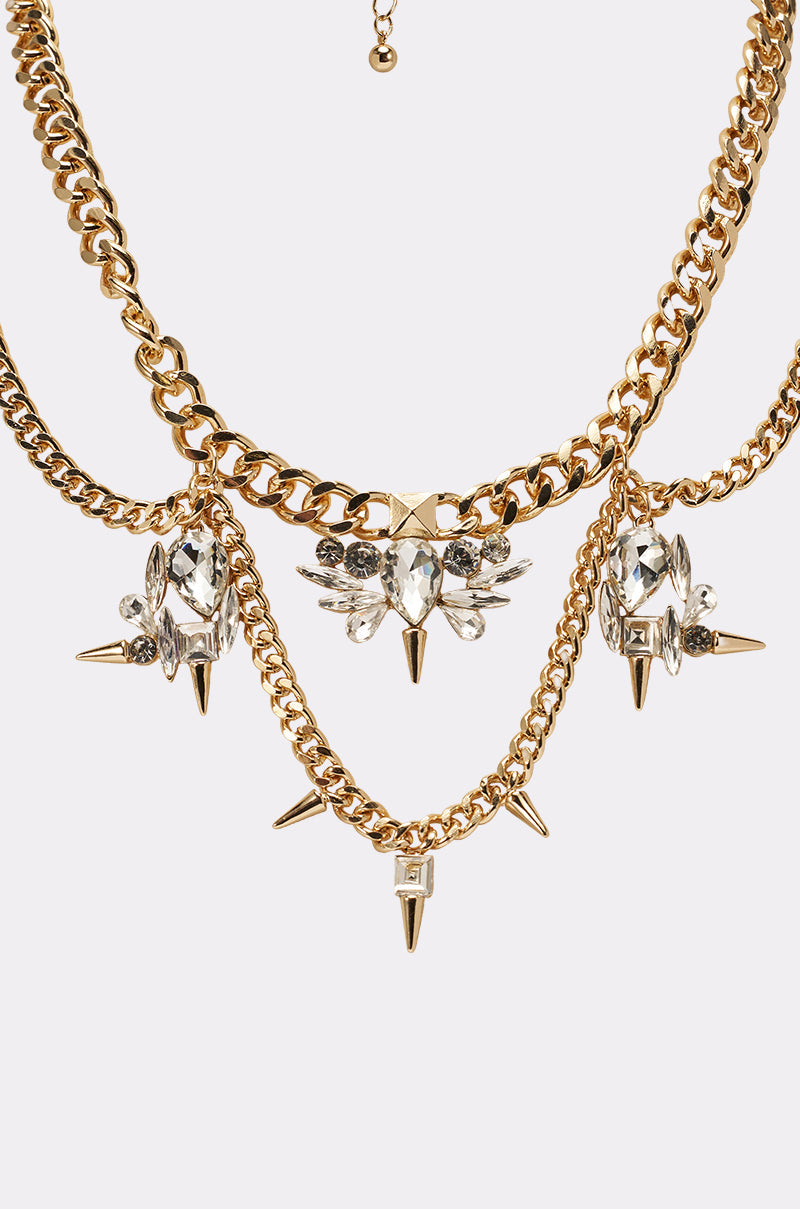 The SPIKEY NECKLACE features bold layered curb-link chains with large clear gemstones, crystal clusters, and gold spike accents for a striking, luxurious style. 3