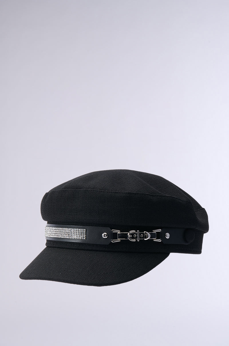 The ITS GIVING BLING BAKER HAT is a stylish black newsboy cap featuring rhinestone embellishments and a small strap with a metal buckle, displayed against a simple gray background. 5
