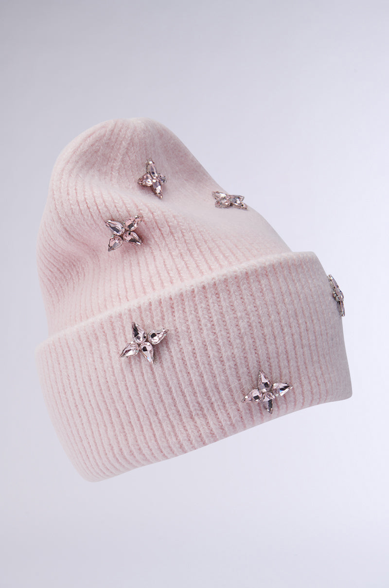 The STAR POWER RHINESTONE BEANIE, a pink ribbed knit accessory from the AKIRA Label, features small sparkling star-shaped rhinestones set against a light grey background. It appears soft and cozy, with intricate embellishments that add an elegant touch.