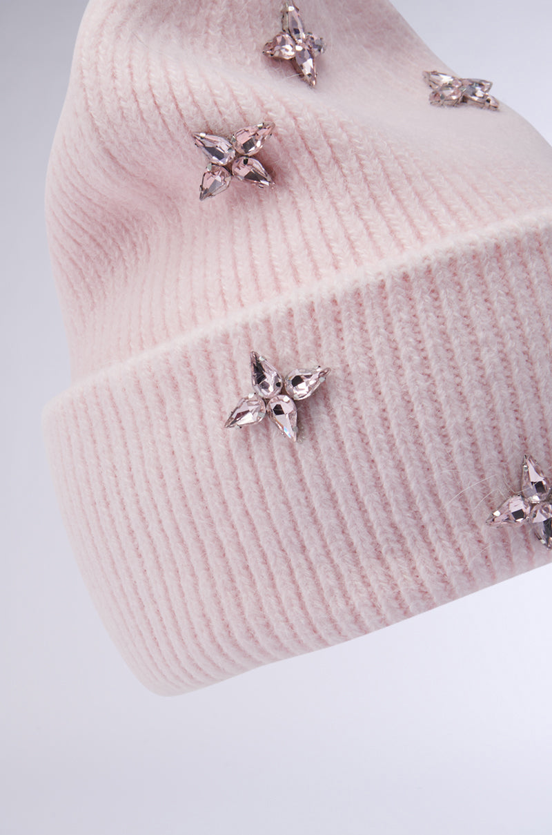 The STAR POWER RHINESTONE BEANIE, a pink ribbed knit beanie, is beautifully embellished with sparkling flower-shaped rhinestones and displayed against a plain gray backdrop. Its folded edge provides an elegant finish to this winter accessory.