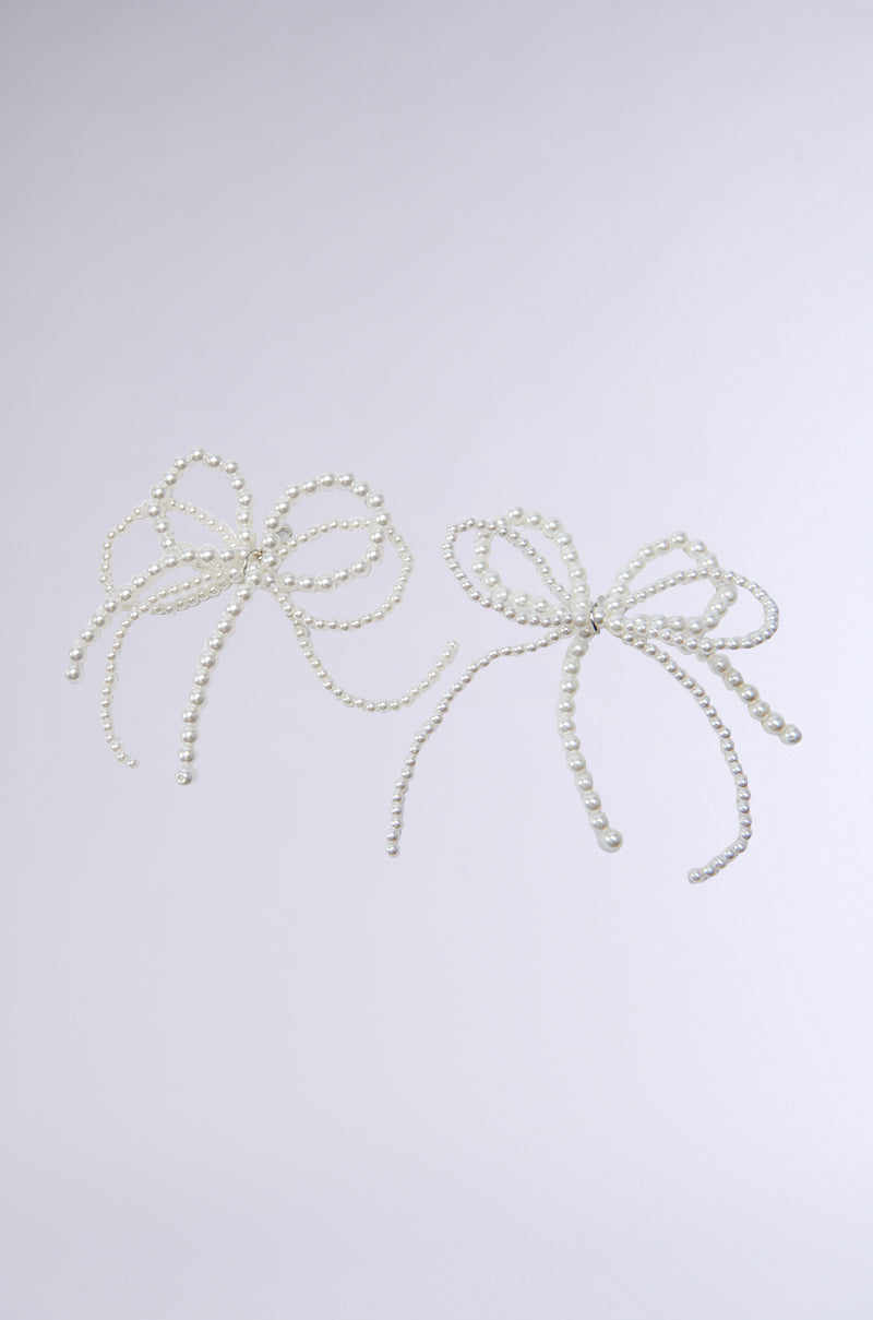 Two COQUETTE CLIP ON CHARMS featuring delicate pearl bows, set against a simple, light background. Each bow is crafted from small faux pearl beads that form graceful, ribbon-like loops.