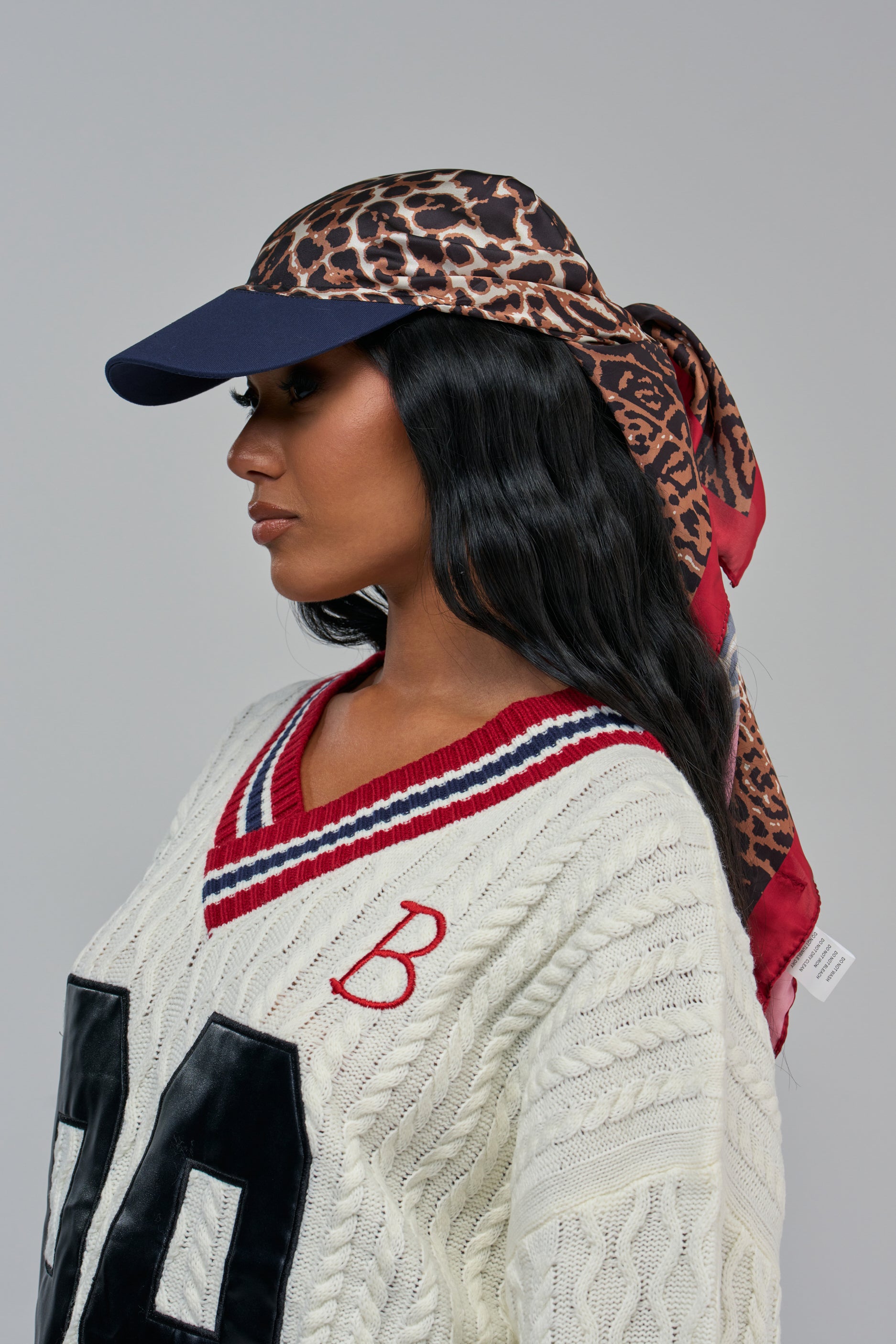 A person wears the IN MY ELEMENT HAT, a leopard-print satin wrap hat featuring a baseball cap base with a scarf tied at the back.