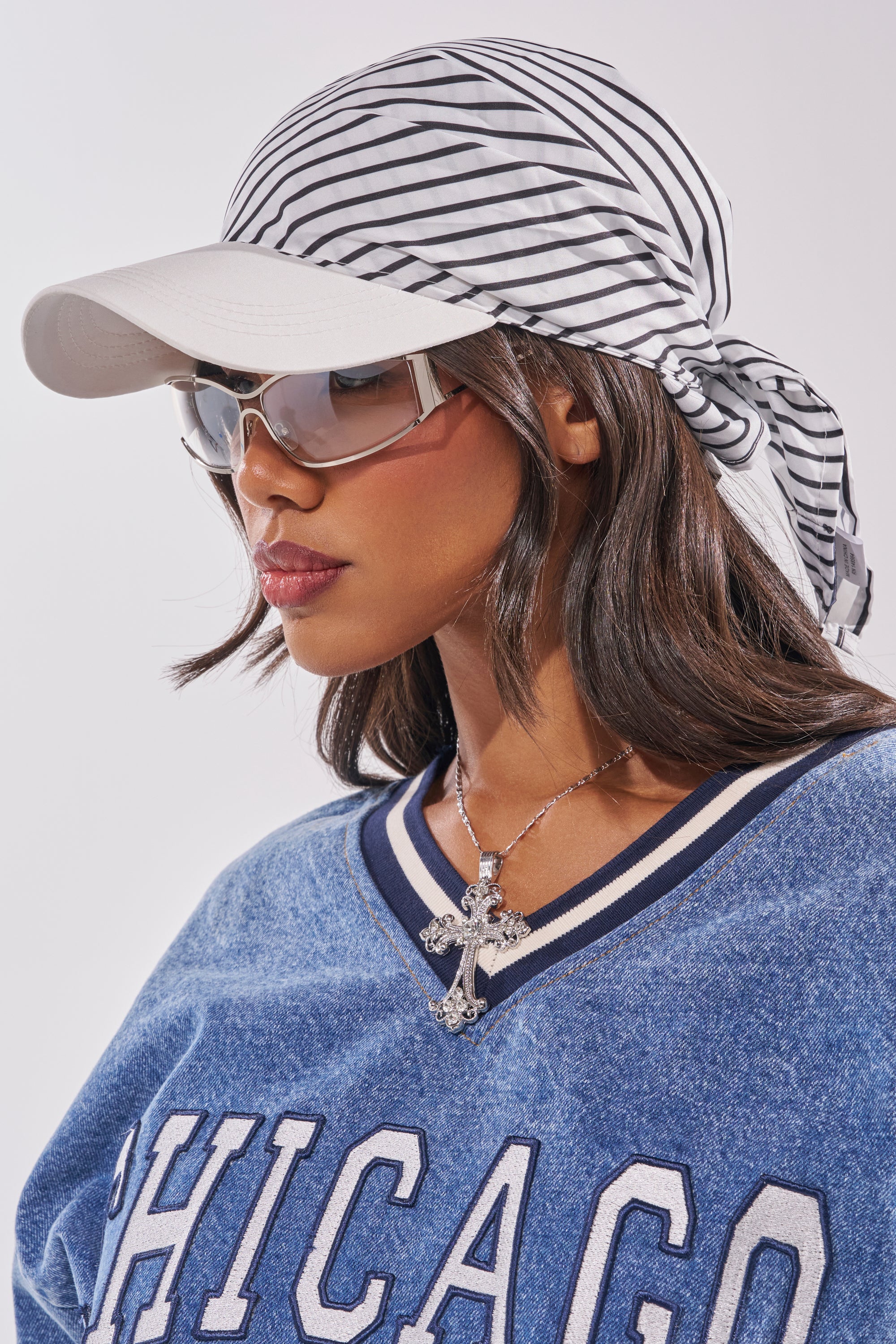Woman wearing the TIED UP HAT over a white cap, large sunglasses, a blue "CHICAGO" jersey, and a cross necklace, looking to the side against a plain background. 0