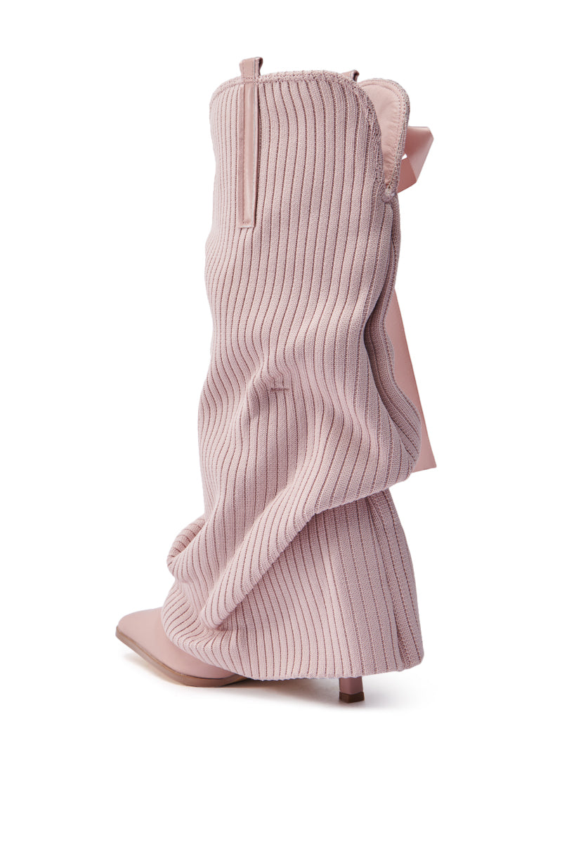 The CODEWORDS PINK BOW STILETTO FOLD OVER BOOT, made from vegan leather, features a single pink high heel with a unique slouchy ribbed fabric, pointed toe, and decorative bow on the back. The thin heel matches the fabric's color and is displayed side-on against a white background.