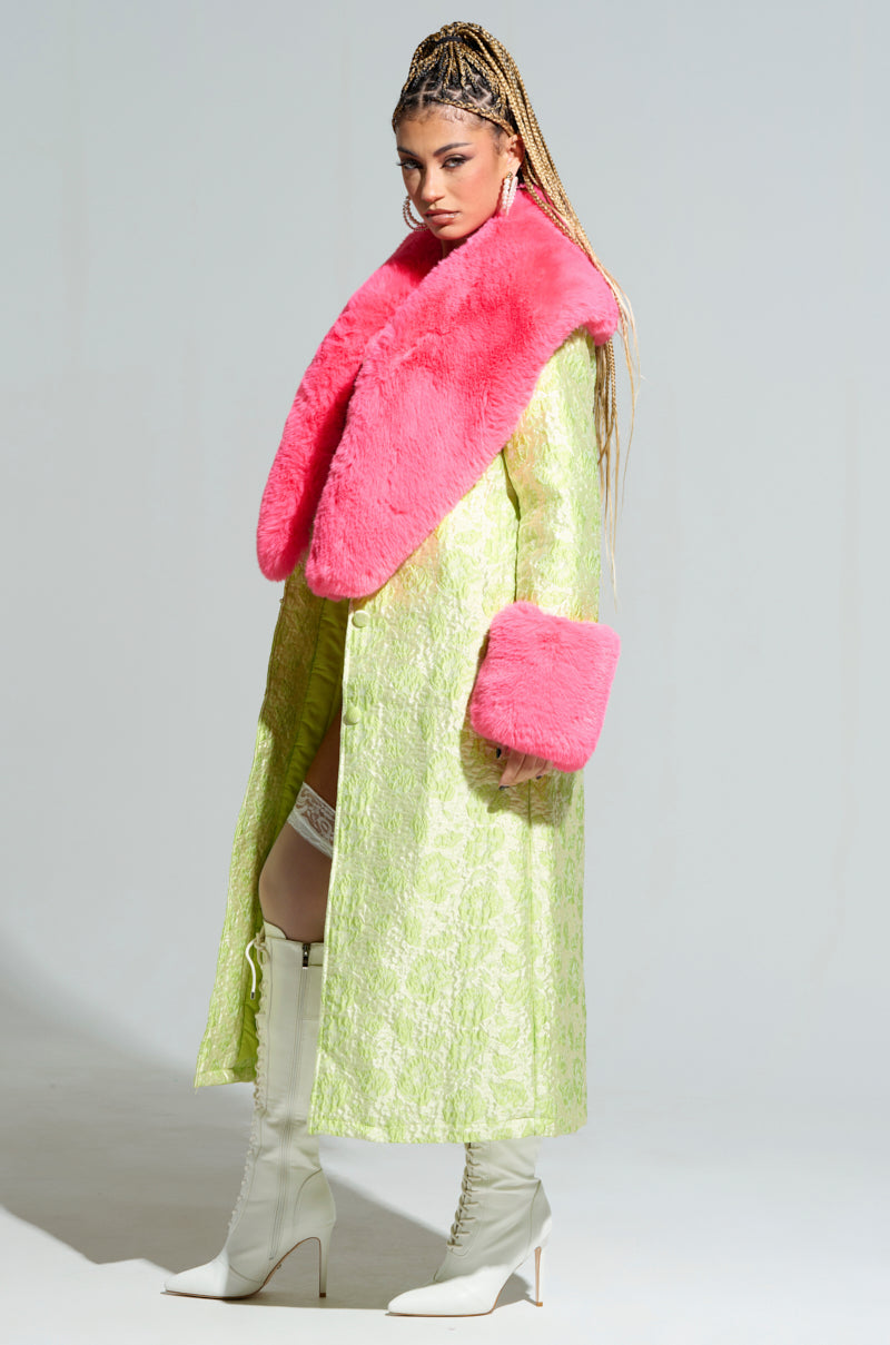Dressed confidently in a textured lime green coat, highlighted by a bright pink faux fur collar and matching vibrant cuffs, they exude style. Their long braided hair frames Y2K-inspired earrings, and white knee-high boots add the finishing touch—a testament to the flair of the "Color Me Pretty Brocade Trench. 3